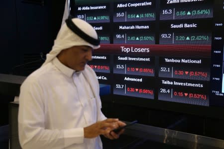 Man walks next to a screen with Saudi Stock Exchange (Tadawul) prices in Riyadh