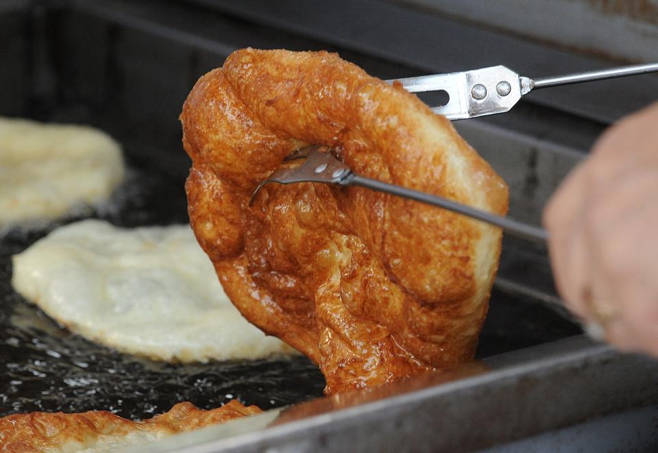 A perfectly fried, golden brown malassada is removed from hot oil at a Portuguese feast.