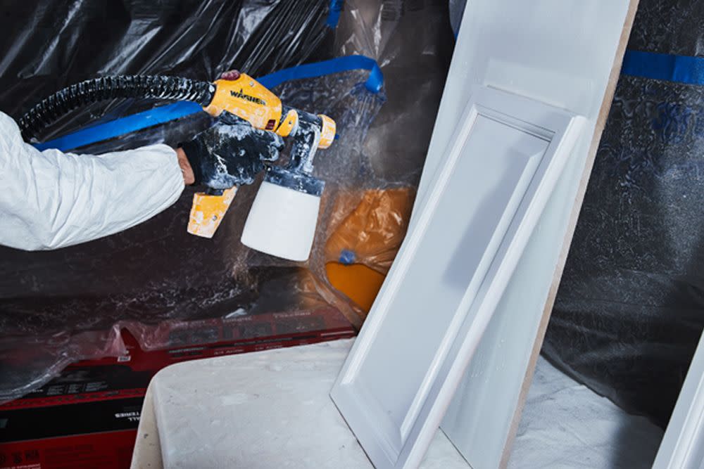 a person adding coats of paint to a section of the kitchen cabinets