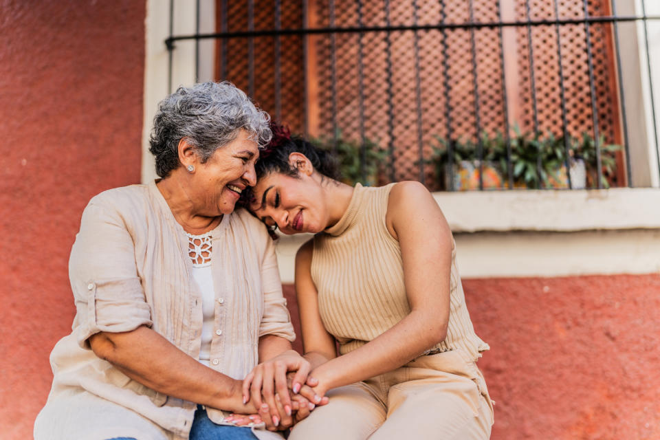 Two women sitting close, one with grey hair, both smiling and holding hands, showing affection and comfort