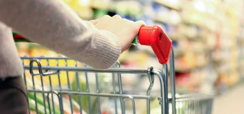 Hands pushing shopping cart down an aisle.