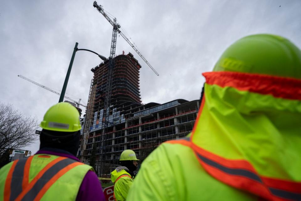 Construction workers gather outside of the Oakridge Mall site after a load on a crane fell off smashing multiple floors of the building in Vancouver, B.C. on Wednesday, Feb. 21, 2024.