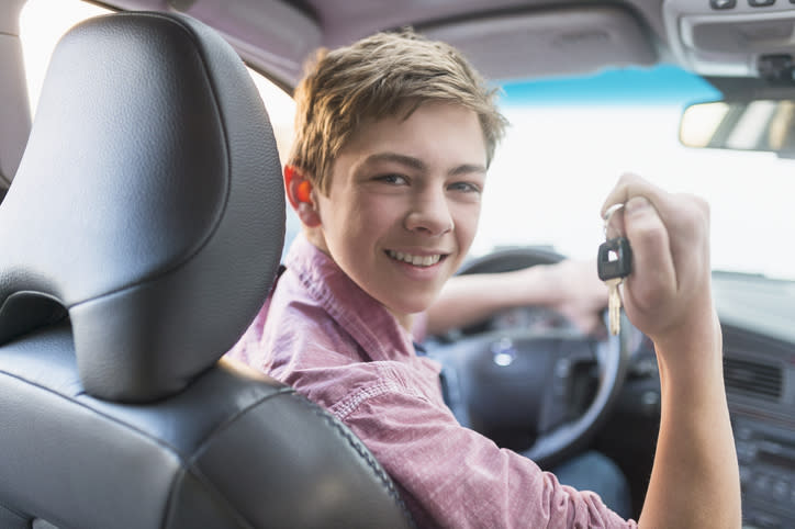 A young teen smiling and holding his car keys while in the driver's seat