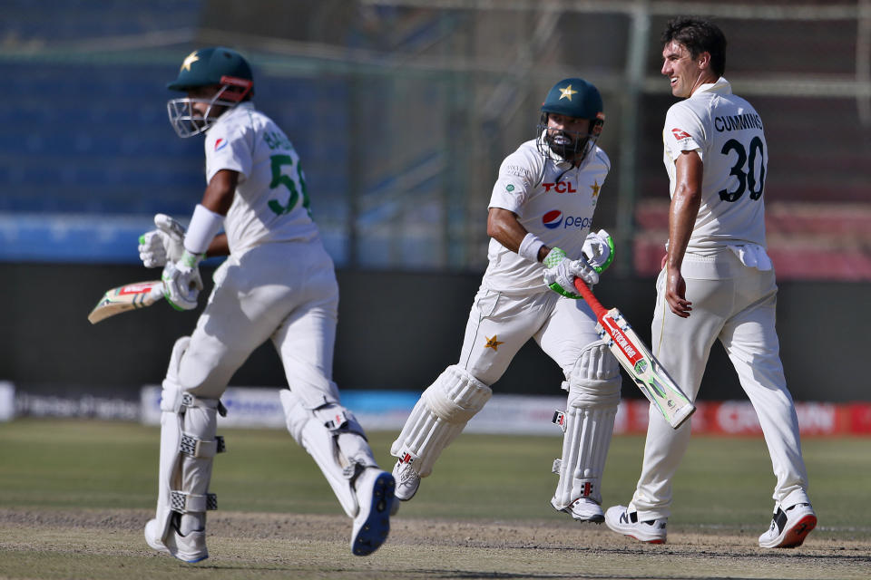 Pakistan's Babar Azam, left, and Mohammad Rizwan run between the wickets while Australia's Pat Cummins watches on the fifth day of the second test match between Pakistan and Australia at the National Stadium in Karachi Pakistan, Wednesday, March 16, 2022. (AP Photo/Anjum Naveed)