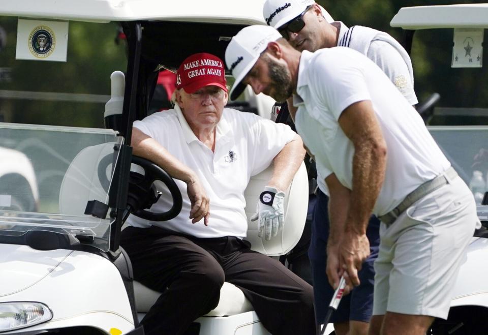 Former President Donald Trump sits in a golf cart as he watches Dustin Johnson putt