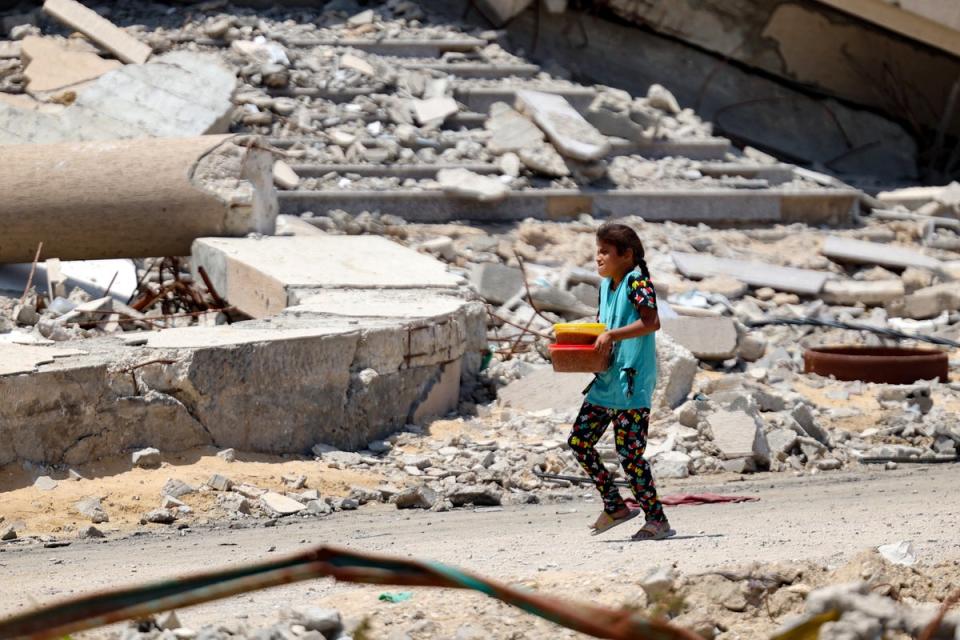 A Palestinian child transporting portions of food walks past a building destroyed by Israeli bombardment in Gaza City in May (Getty)