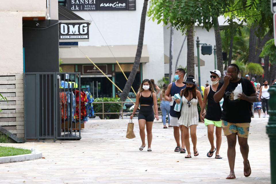 People walk past shops in the Waikiki neighborhood of Honolulu, Tuesday, Aug. 24, 2021. Hawaii was once seen as a beacon of safety during the pandemic because of stringent travel and quarantine restrictions and overall vaccine acceptance that made it one of the most inoculated states in the country. But the highly contagious delta variant exploited weaknesses as residents let down their guard and attended family gatherings after months of restrictions and vaccine hesitancy lingered in some Hawaiian communities.(AP Photo/Caleb Jones)