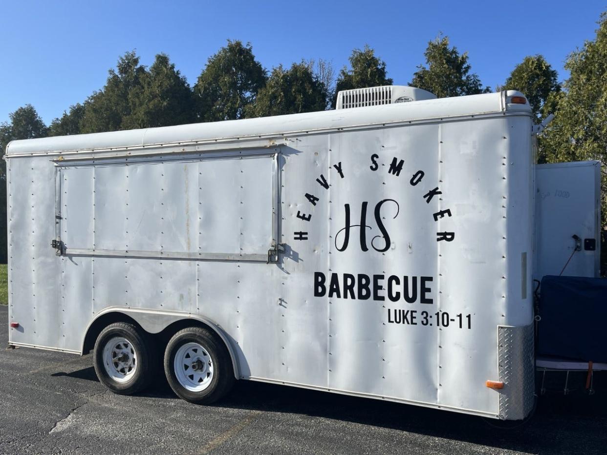 The side of the Heavy Smoker BBQ truck parked in the Breaking Bread parking lot depicts a Bible verse in black vinyl.