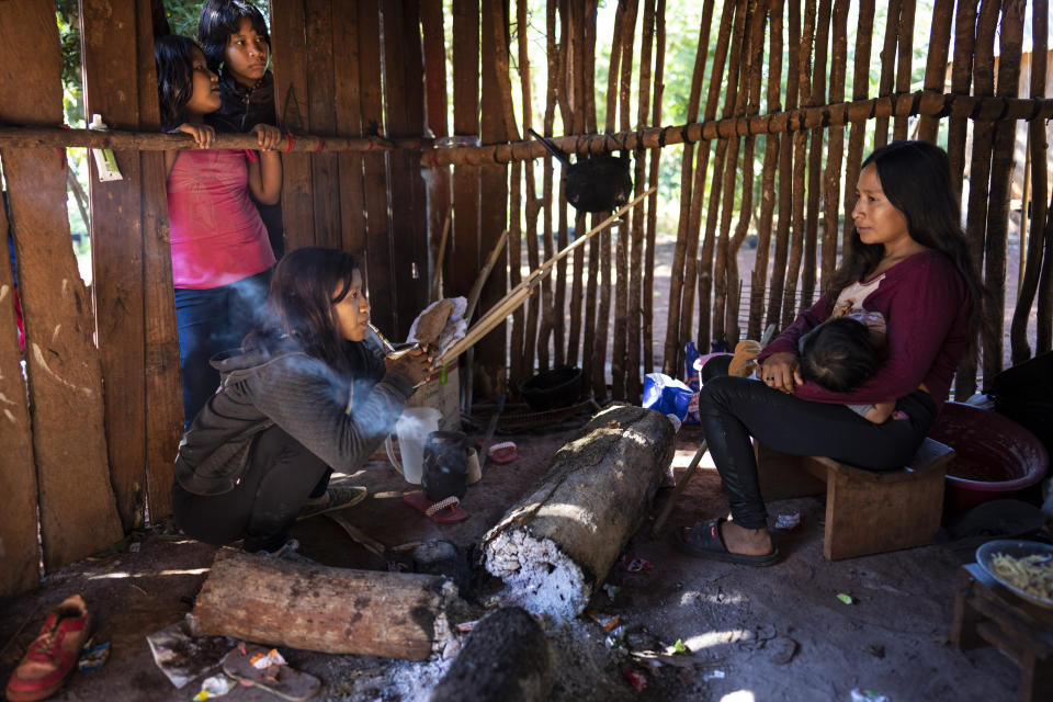 Margarita Mendez, frente, izquierda, bebe mate mientras su amiga Cristina Chamorro da el pecho a su hijo en una cocina al aire libre en la comunidad indígena guaraní de Kaaguy Pora II, en las afueras de Andresito, en la provincia argentina de Misiones, el centro de la producción mundial de mate, el jueves 18 de abril de 2024. La yerba mate se encuentra en casi todos los hogares argentinos. (AP Foto/Rodrigo Abd)