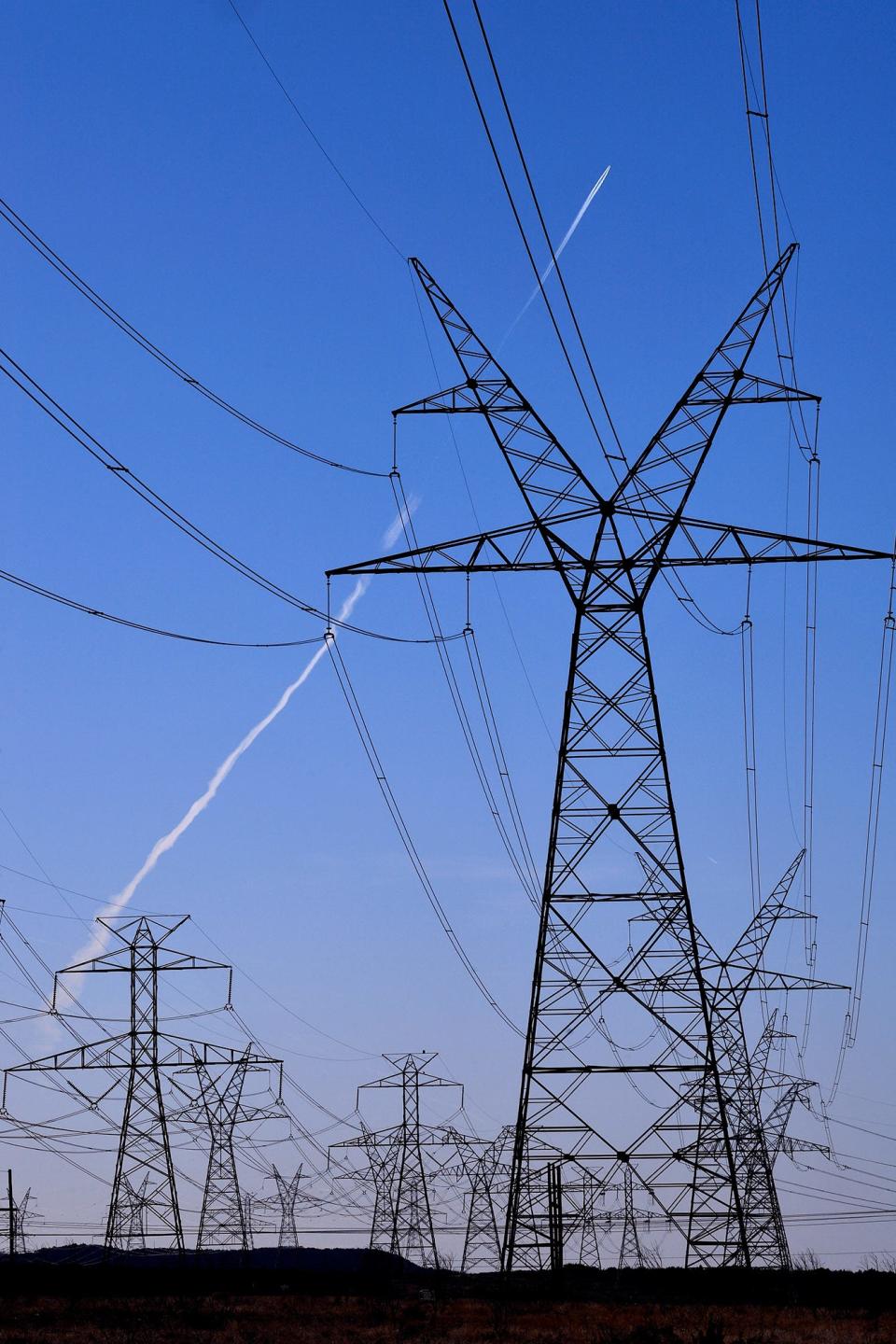 An aircraft contrail traces a white line in the sky beyond electrical transmission lines in south Taylor County, Texas on Jan. 15, 2021. The towers were part of the CREZ, or Competitive Renewable Energy Zones, project which was completed in 2013 to transmit electricity from West Texas wind turbines to central and eastern parts of the state. 