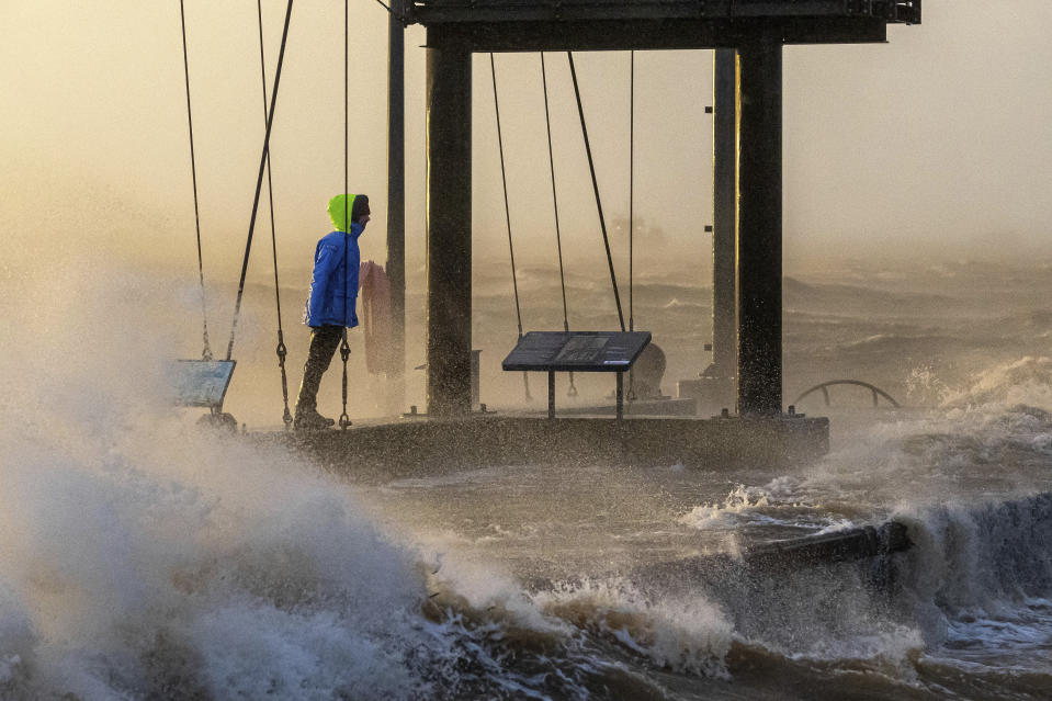 A person walks along the banks of the Weser estuary during a storm surge and waves in Bremerhaven, Germany, Friday Dec. 22, 2023. Pre-Christmas rail travelers in parts of Germany faced widespread disruption on Friday as a storm swept across northern Europe, bringing down trees and prompting warnings of flooding on the North Sea coast. (Sina Schuldt/dpa via AP)