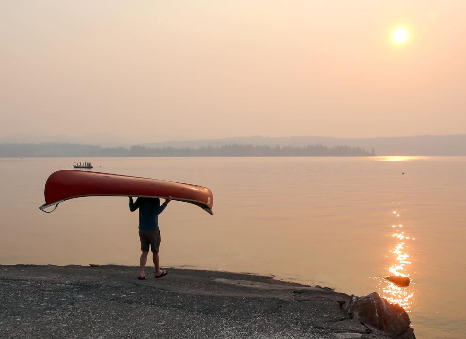 David Presley carries a canoe down the Tracyton Boat Launch as thick wildfire smoke hangs in the air on Sunday, Aug. 20, 2023.