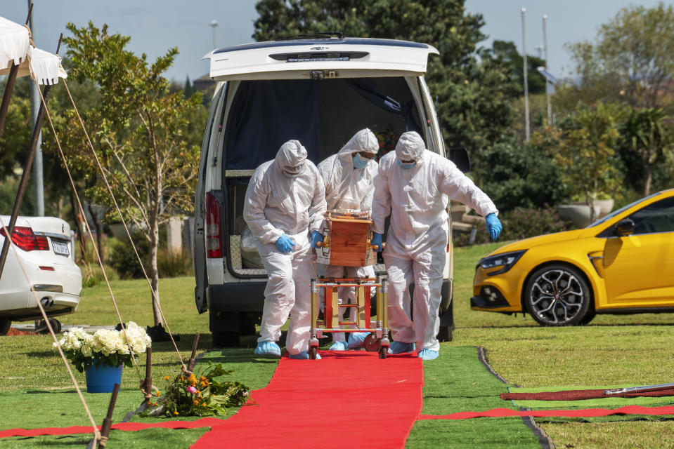 Pallbearers wearing full PPE suits lift the casket containing the remains of Benedict Somi Vilakasi for his burial ceremony at the Nasrec Memorial Park outside Johannesburg Thursday, April 16, 2020. Vilakasi, a Soweto coffee shop manager, died of Covid-19 infection in a Johannesburg hospital Sunday April 12 2020. South Africa is under a strict five-week lockdown in a effort to fight the Coronavirus pandemic.(AP Photo/Jerome Delay)