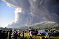 People watch as Mount Sinabung spews volcanic material during an eruption in Karo, North Sumatra, Indonesia, Tuesday, March 2, 2021. The 2,600-metre (8,530-feet) volcano erupted Tuesday, sending volcanic materials a few thousand meters into the sky and depositing ash on nearby villages. (AP Photo)