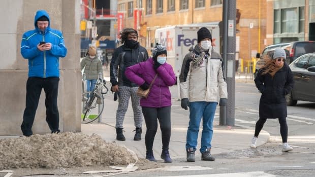 Pedestrians wait to cross an intersection in downtown Toronto on Monday. Environment Canada issued a special weather statement warning of winds gusting up to 80 km/h on Monday afternoon.  (Sam Nar/CBC - image credit)