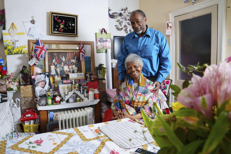 Sylius and Bridgette Toussaint pose for a photo, at their home in Preston, England, Tuesday, April 25, 2023. King Charles III will be crowned Saturday, May 6, 2023 at Westminster Abbey in an event full of all the pageantry Britain can muster. Sylius Toussaint and his wife, Bridgette, will be watching. The couple celebrated Elizabeth’s coronation as children on the island of Dominica and moved to England in 1960 to find work. A corner of their home in Preston is festooned with royal photos and souvenirs, including a tin of coronation shortbread. (AP Photo/Jon Super)