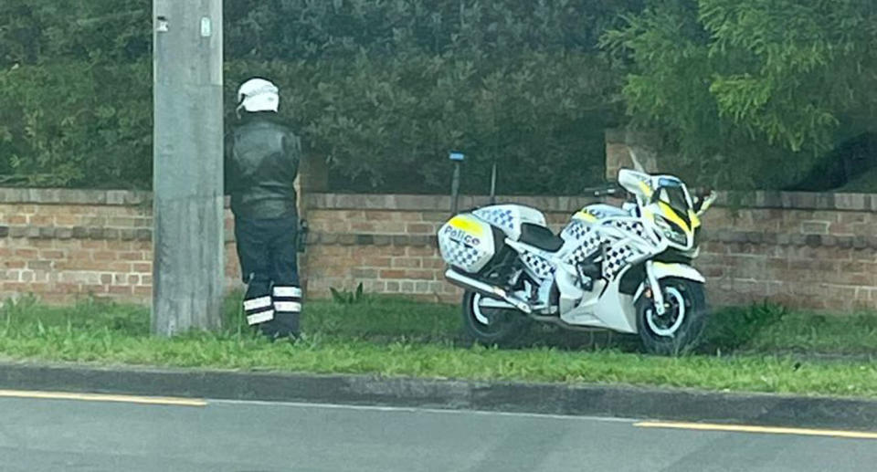  NSW police officer standing being pole with motorcycle on footpath.