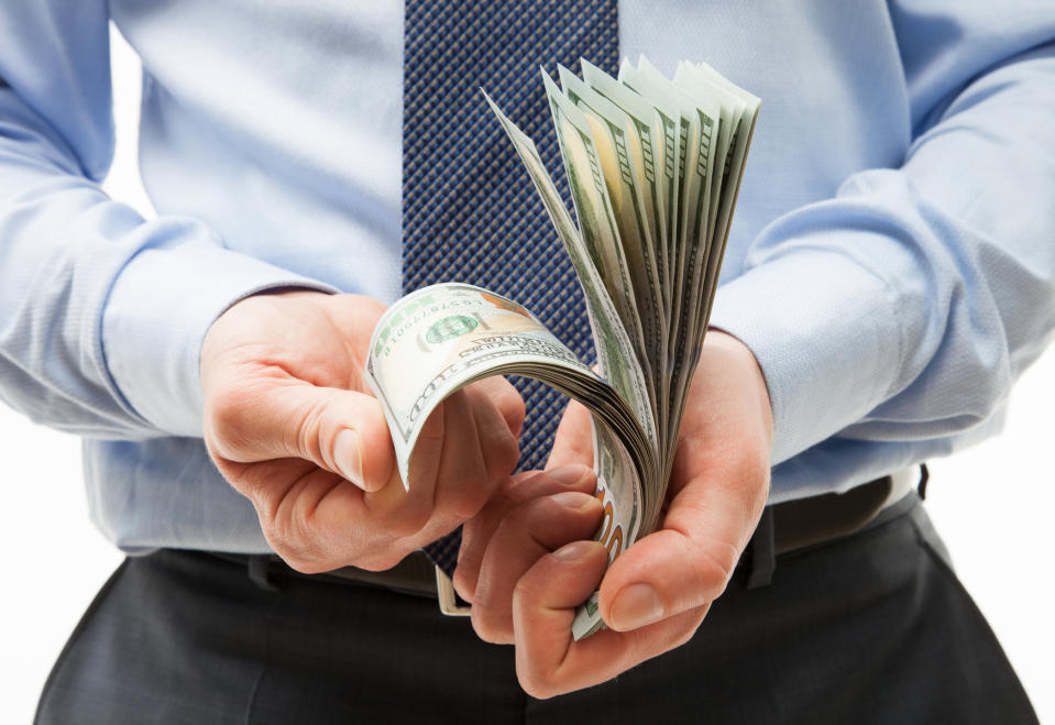 A businessmen with a dress shirt and tie counting a pile of cash in his hands.