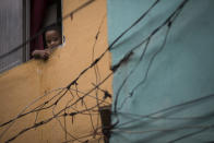 A young resident looks out from his window as military police officers patrol during an operation in the Mare slum complex, ahead of its "pacification," in Rio de Janeiro, Brazil, Tuesday, March 25, 2014. Elite federal police and army troops will be sent to the city to help quell a wave of violence in so-called "pacified" slums. Recent attacks on police bases in the favelas is raising concerns about an ambitious security program that began in 2008, in part to secure the city ahead of this year's World Cup and the 2016 Olympics. (AP Photo/Felipe Dana)