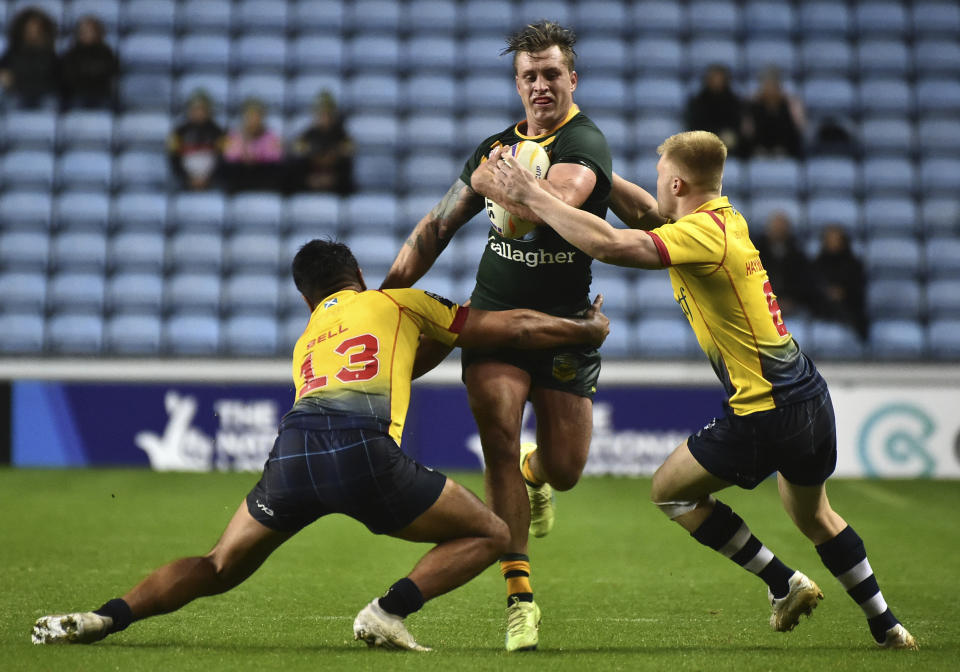 Australia's Cameron Munster, middle, is tackled by Scotland's James Bell, left, and teammate Bailey Hayward during the Rugby League World Cup match between Australia and Scotland at Coventry Building Society Arena, Coventry, England, Friday, Oct. 21, 2022. (AP Photo/Rui Vieira)