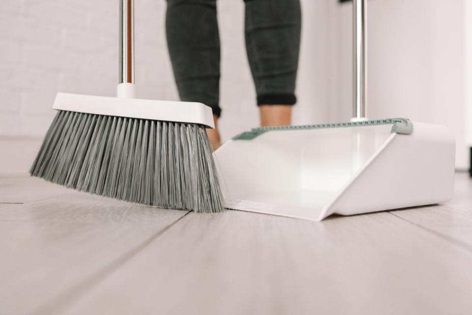 Broom and dustpan sweeping a laminate floor.