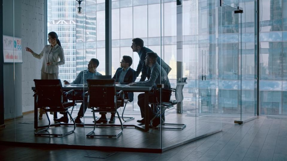 Four people in a conference room look at a presentation.