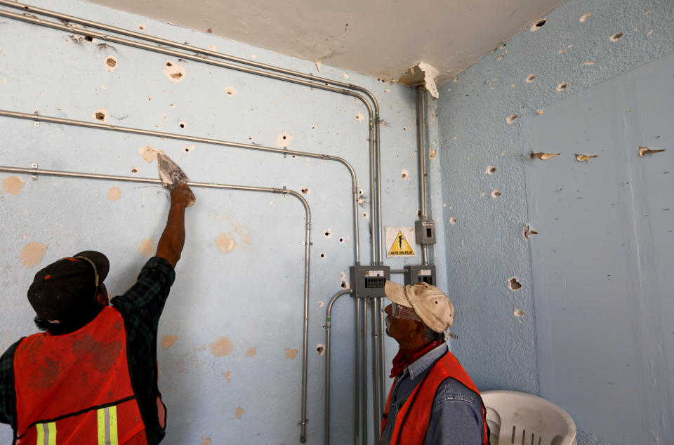 A worker repairs a wall riddled with bullet holes at City Hall in Villa Union, Mexico, Monday, Dec. 2, 2019. The small town near the U.S.-Mexico border began cleaning up Monday even as fear persisted after 22 people were killed in a weekend gun battle between a heavily armed drug cartel assault group and security forces. (AP Photo/Eduardo Verdugo)