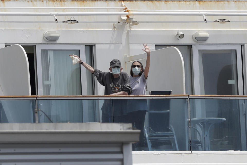 Passengers wearing protective masks wave to members of the news media as they stand on their balcony aboard the Coral Princess cruise ship while docked at PortMiami during the new coronavirus outbreak, Monday, April 6, 2020, in Miami. According to Princess Cruises, disembarkation of guests is expected to take several days due to limited flight availability. (AP Photo/Wilfredo Lee)