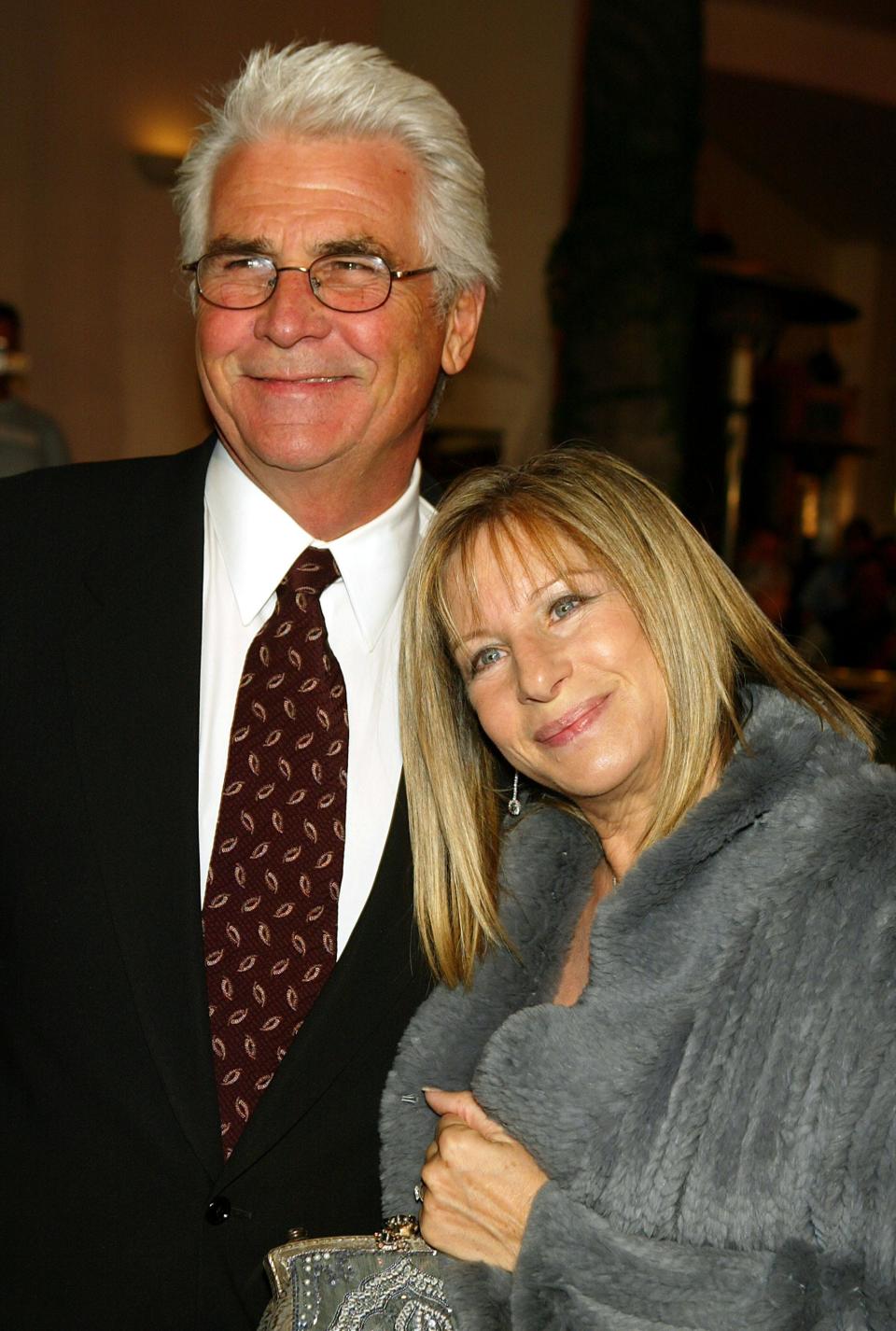 James Brolin, in a black suit, white shirt, red tie, and glasses, poses with Barbra Streisand, in a gray fur coat.