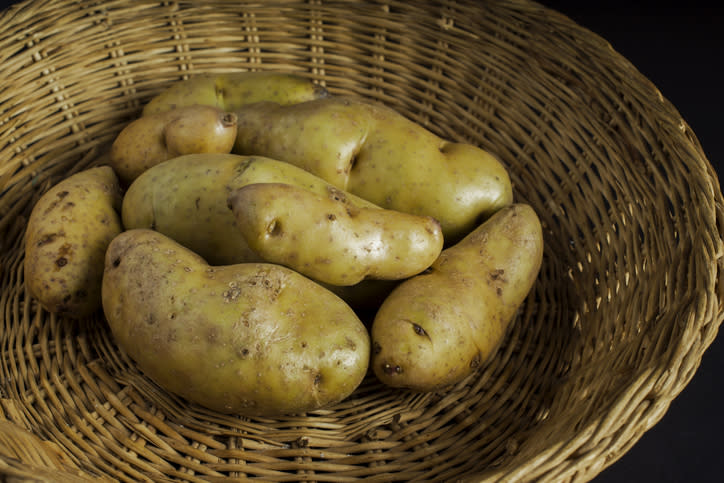 A wicker basket filled with multiple unpeeled potatoes