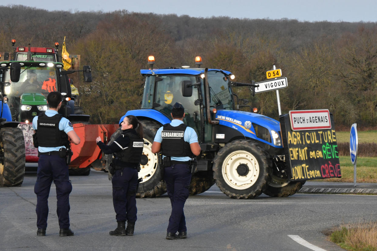 Des gendarmes montent la garde alors que des tracteurs roulent sur une route à Vigoux, le 30 janvier 2024, en direction du marché de gros de Rungis.