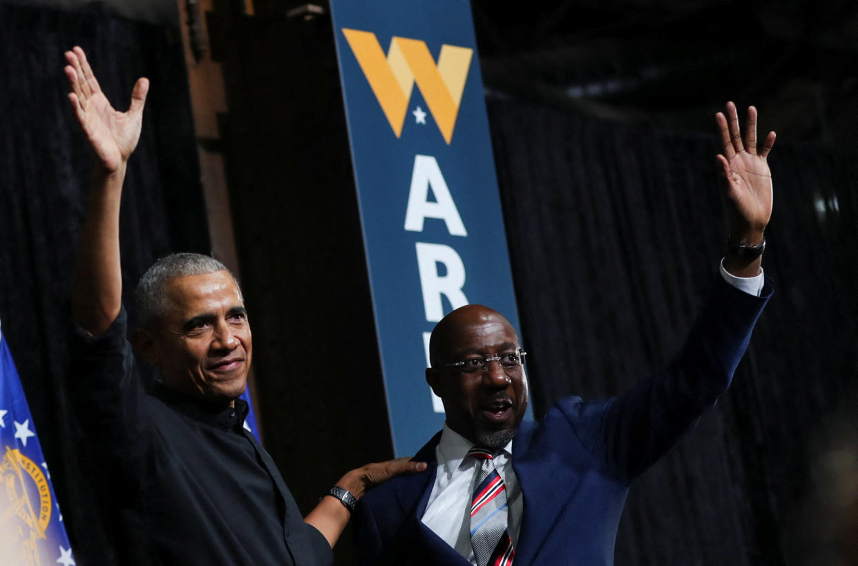 Former President Barack Obama and Senator Raphael Warnock wave to the audience during a campaign rally.