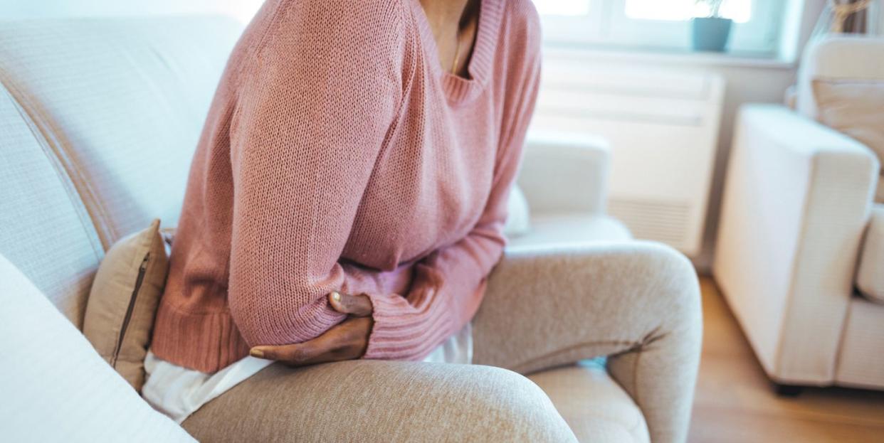 woman sitting on sofa holding stomach hunched in pain