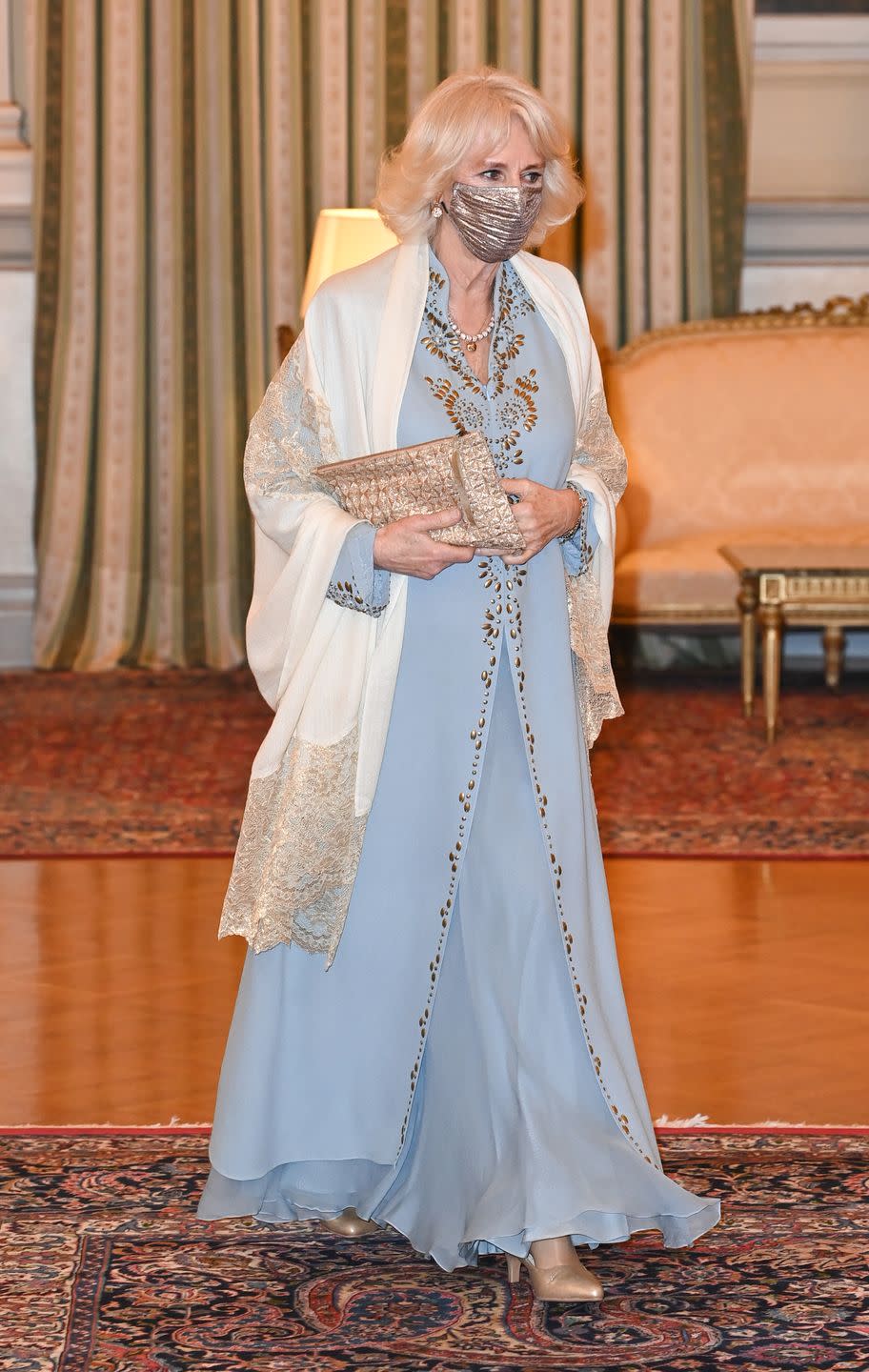 <p>The Duchess of Cornwall stunned in a flowy light blue dress with gold detailing and a cream lace shawl for a reception on the first day of <a href="https://www.townandcountrymag.com/society/tradition/a35886831/prince-charles-camilla-royal-tour-greece-2021/" rel="nofollow noopener" target="_blank" data-ylk="slk:a trip to Athens;elm:context_link;itc:0;sec:content-canvas" class="link ">a trip to Athens</a> in <a href="https://www.townandcountrymag.com/society/tradition/g35936585/prince-charles-camilla-greece-photos-march-2021/" rel="nofollow noopener" target="_blank" data-ylk="slk:celebration of the 200th anniversary of Greek independence;elm:context_link;itc:0;sec:content-canvas" class="link ">celebration of the 200th anniversary of Greek independence</a>. She chose a matching shimmery gold clutch and a metallic gold face mask for the occasion, which was hosted by the President of Greece.</p>