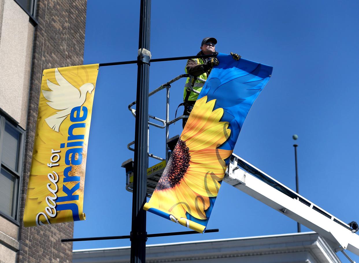 Ace Sign Co. of Springfield employee Ben Poteet hangs a 'Peace for Ukraine" banner on a light pole at the corner of South Fifth Street and East Washington Street on Tuesday April 19, 2022. [Thomas J. Turney/ The State Journal-Register]