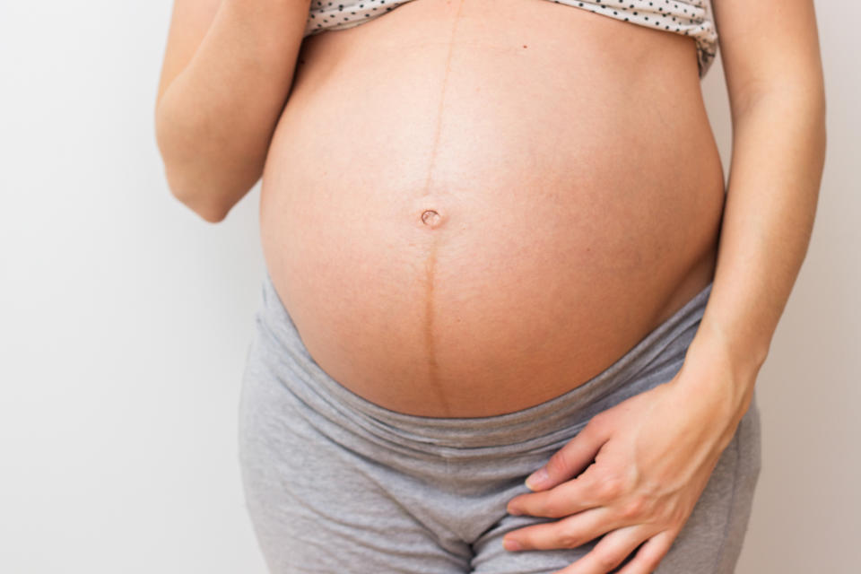 Pregnant beautiful woman holds hands on belly at home interiors. Pregnant woman standing next to wall