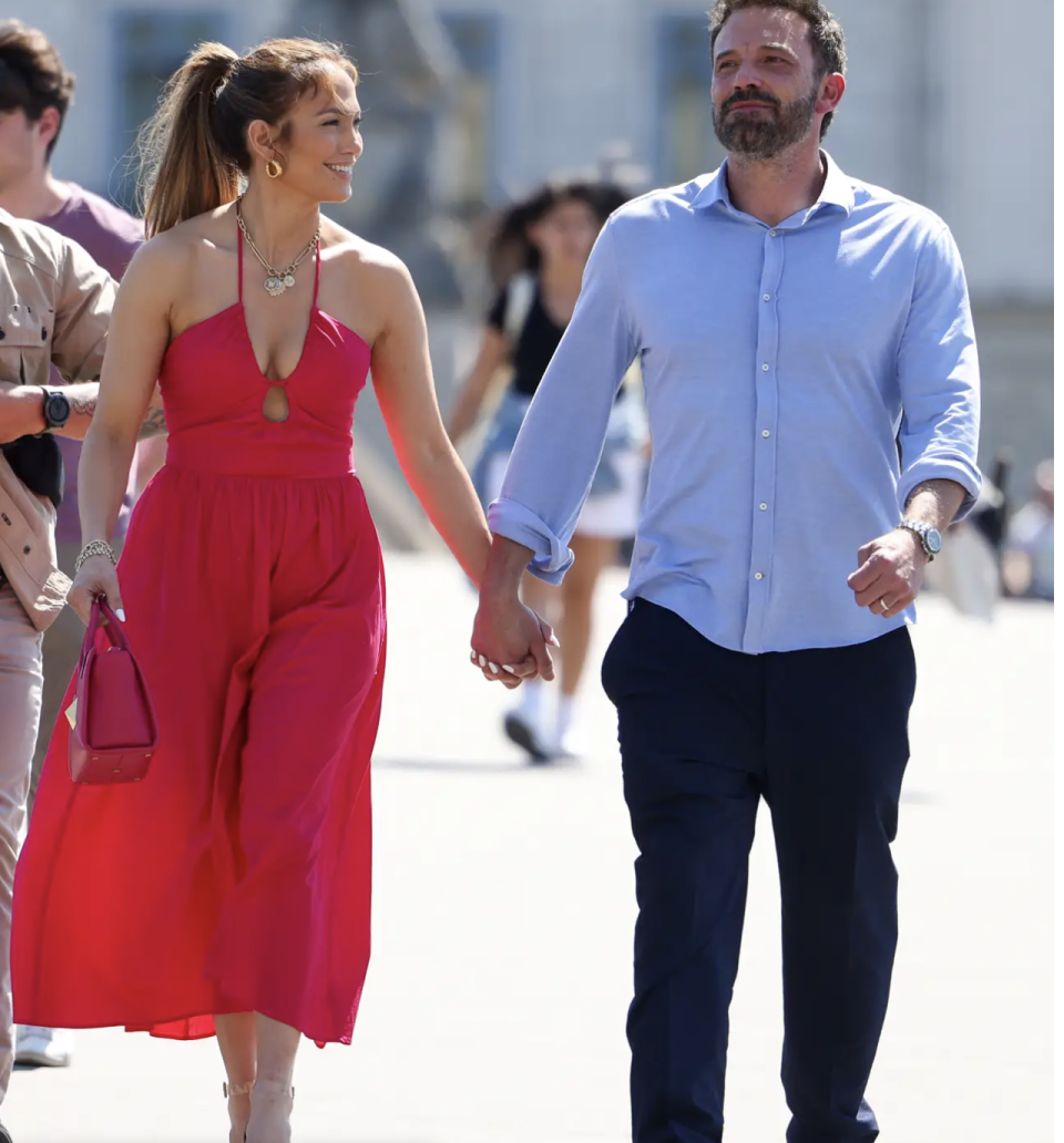 Jennifer Lopez and Ben Affleck walking together hands clasped on their recent honeymoon, Jen wears a stunning red halter neck dress while Ben wears black pants with blue shirt with cuffs rolled up