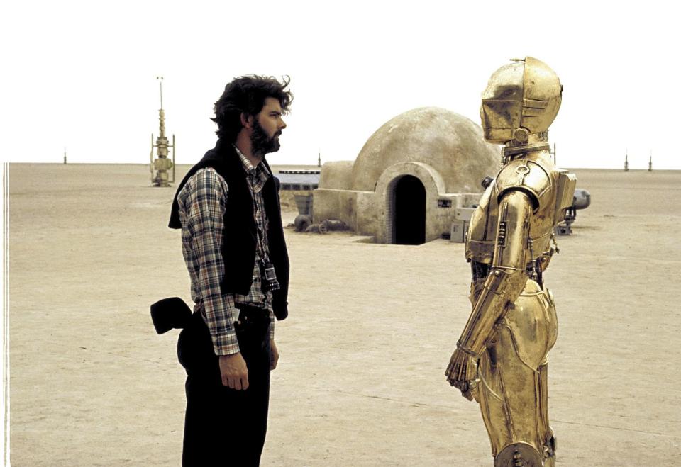 <p>George Lucas unterhält sich am Rande der Dreharbeiten zu “Star Wars: Episode IV – Eine neue Hoffnung” mit C-3PO. Unter dem Blechanzug befindet sich der britische Schauspieler Anthony Daniels, der den Roboter von Anfang an bis hin zum Ableger “Solo: A Star Wars Story” gespielt hat. Auch in Teil neun der Reihe, “Der Aufstieg Skywalkers”, ist er wieder dabei. (Bild: ddp images/Capital Pictures) </p>