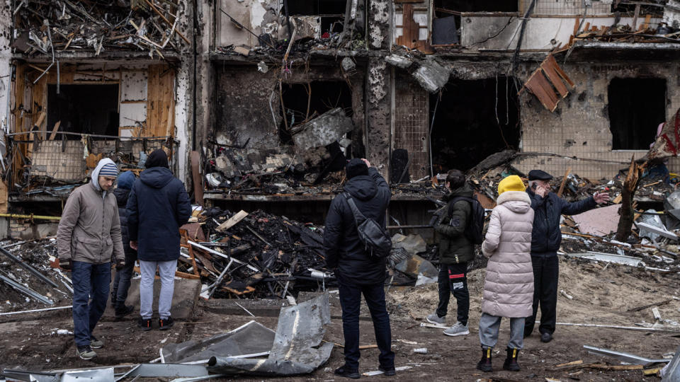 People stand outside a damaged residential building hit by a missile strike.