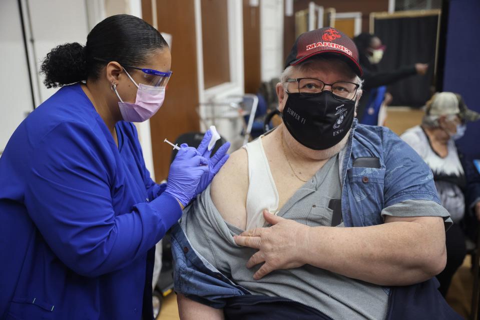 man in a mask getting his third booster shot of Pfizer vaccine injected into his right arm by a healthcare worker (also masked).