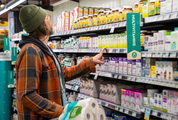 Un acheteur examine une sélection de suppléments vitaminiques dans un magasin.