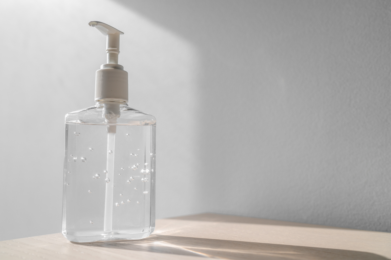 Hand sanitizer in a plastic bottle on a table, on the left, light coming through, a grey wall blurred in the background