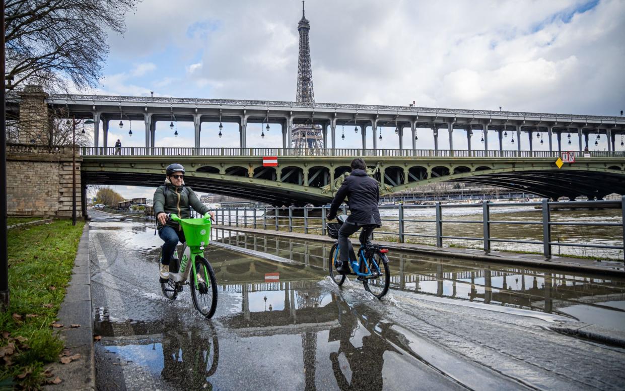 Cyclists ride along the flooded promenade on the bank of the Seine river close to the Eiffel tower