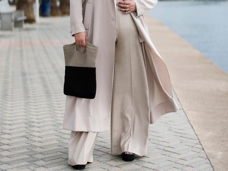 Model wearing a trench coat, wide-leg pants and a handbag.