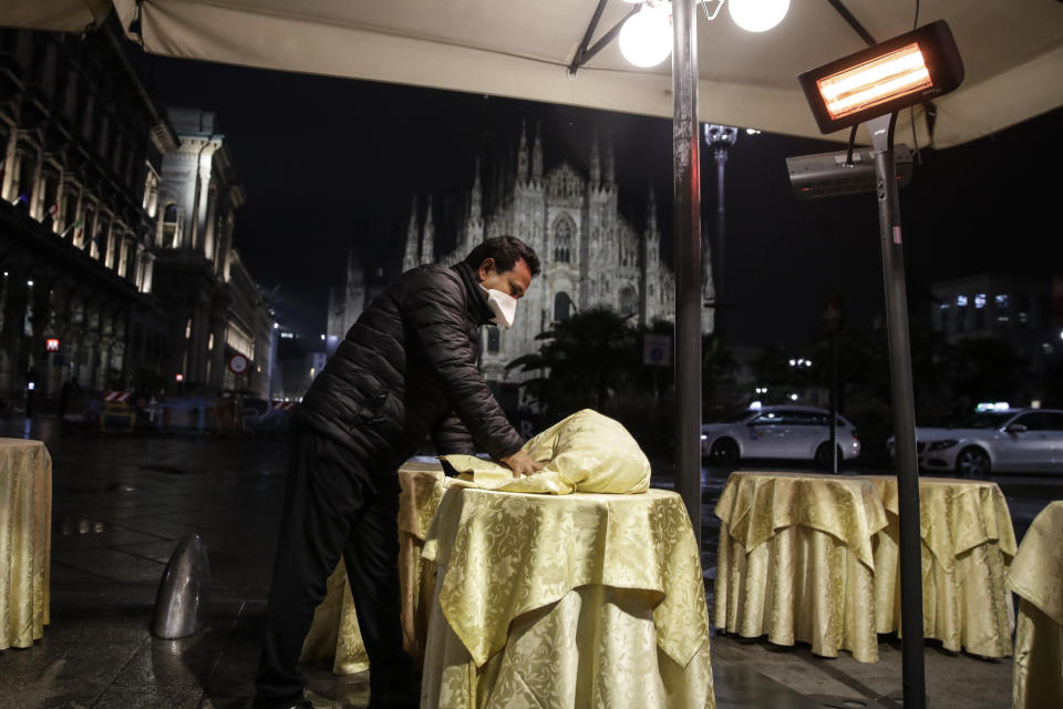 A waiter clears tables at a cafe restaurant in front of the gothic cathedral in Milan, Italy, Thursday, Oct. 22, 2020. Authorities in regions including Italy's three largest cities have imposed curfews in a bid to slow the spread of COVID-19, as many of the cases in Lombardy's surging outbreak have occurred in Milan. On Thursday, an overnight curfew takes effect in the city, known for its lively night-time bar scene, and the rest of the region, as authorities try to slow the spread of the contagion. (AP Photo/Luca Bruno)