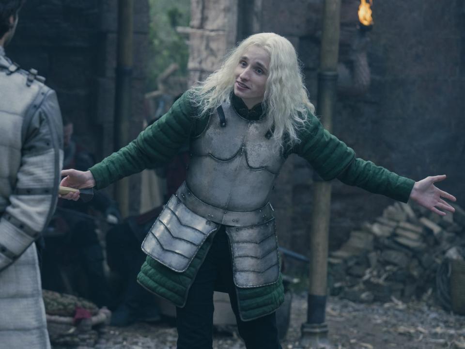 An older teenage boy in a green tunic under silver armor with his hands outstretched.