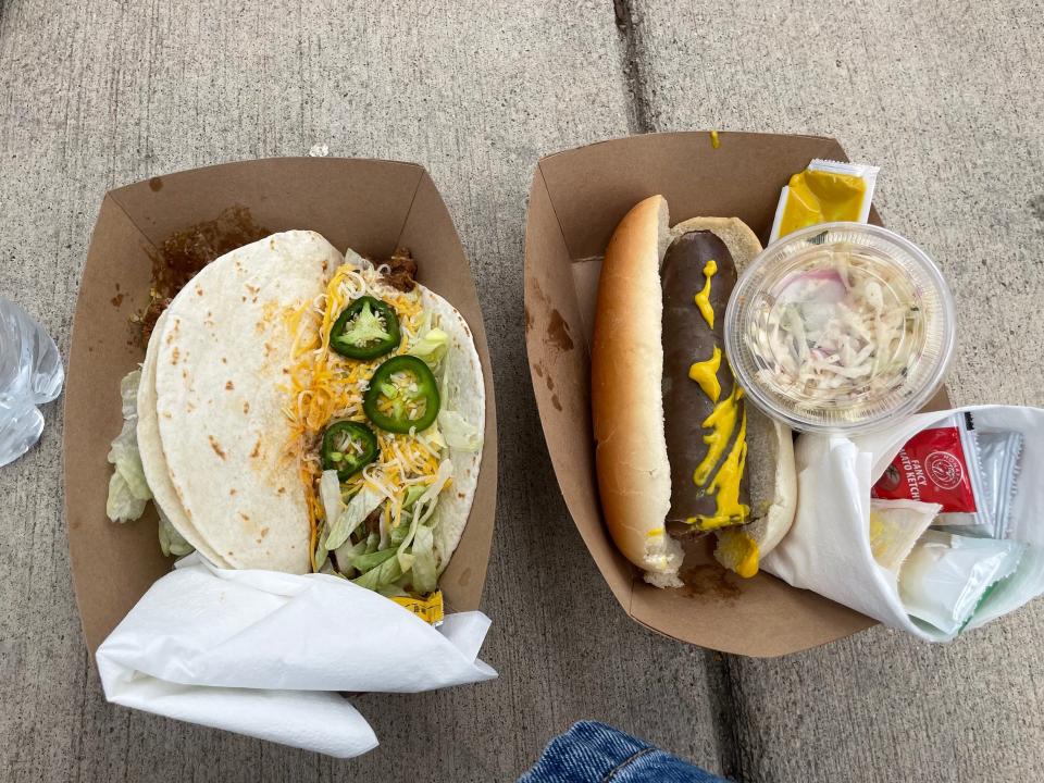 Two cardboard containers on ground, one with tortillas, shredded cheese, and jalapenos next to cardboard box filled with yak bratwurst and sides