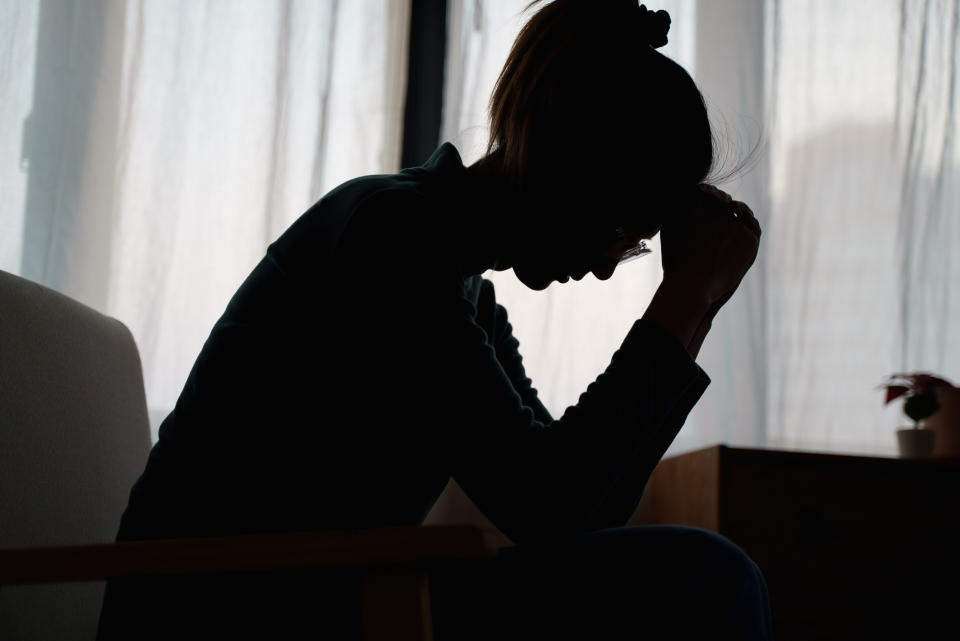 A person sits silhouetted against a light background, leaning forward with their head resting on their hand, conveying a sense of contemplation or stress