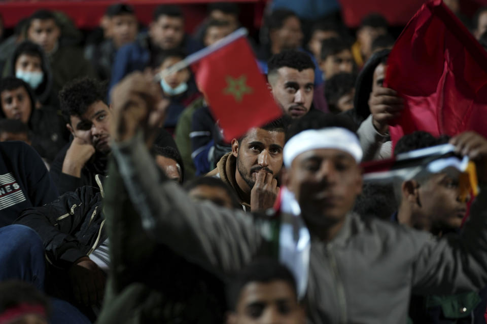 A Palestinian man waves a Moroccan flag as others watch a live broadcast of the World Cup semifinal soccer match between Morocco and France played in Qatar, at the municipality stadium in Rafah refugee camp, Southern Gaza Strip, Wednesday, Dec. 14, 2022. (AP Photo/Adel Hana)