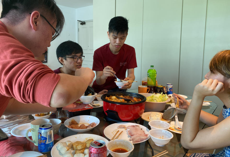 Malaysian students, from left, Felix Mong, Ter Leong Kern and Siew Ee Sung enjoy a Lunar New Year hot pot lunch provided by their Malaysian host Chan Jit Yen, right, at her rented apartment in Singapore, Saturday, Feb. 13, 2021. With Malaysian workers and students stranded in the city state over the Lunar New Year due to coronavirus travel restrictions, the Malaysian Association in Singapore has called on Malaysians to treat students to a meal. (AP Photo/Annabelle Liang)